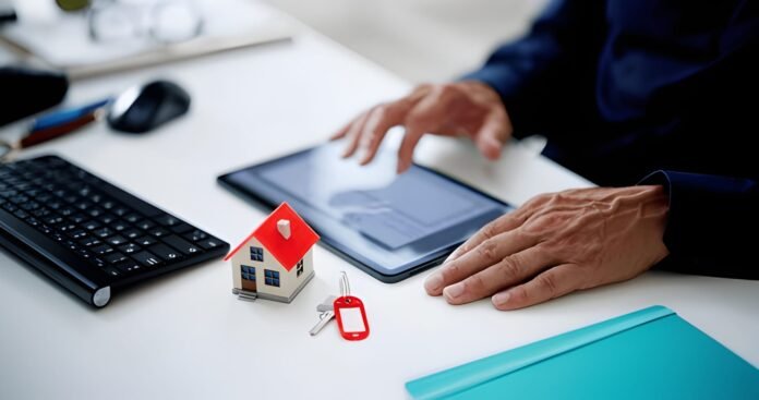 individual reviewing property listings on a laptop or tablet, with a house model or keys on the table